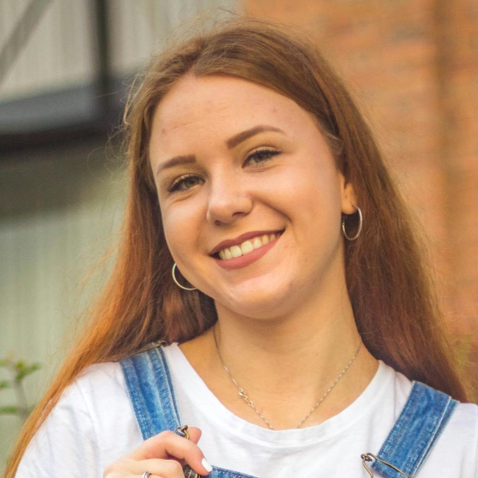 Portrait of a smiling young woman wearing denim overalls in an urban setting.